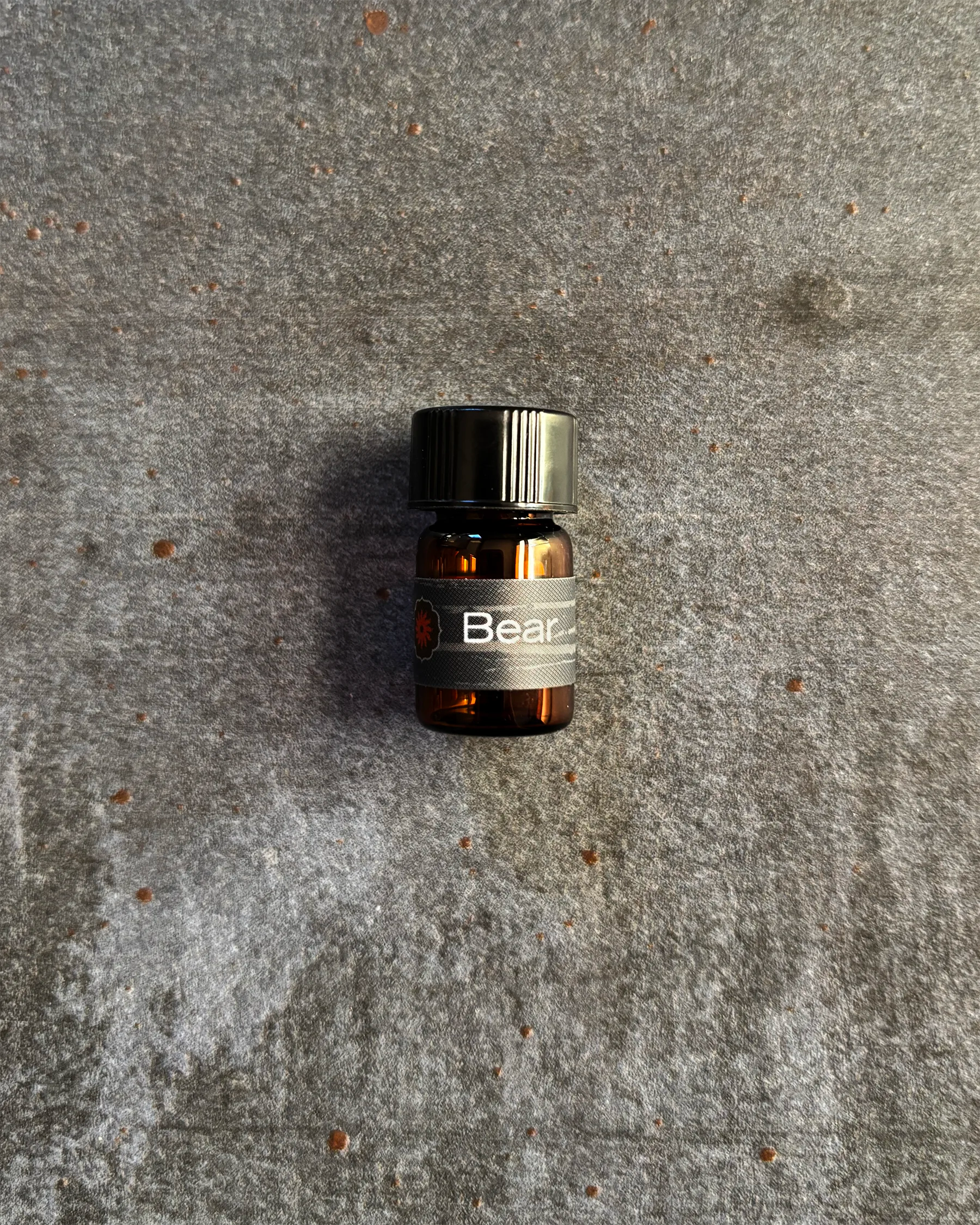 Small amber vial of BodyMantra Bear Power Animal oil blend on textured gray stone background.