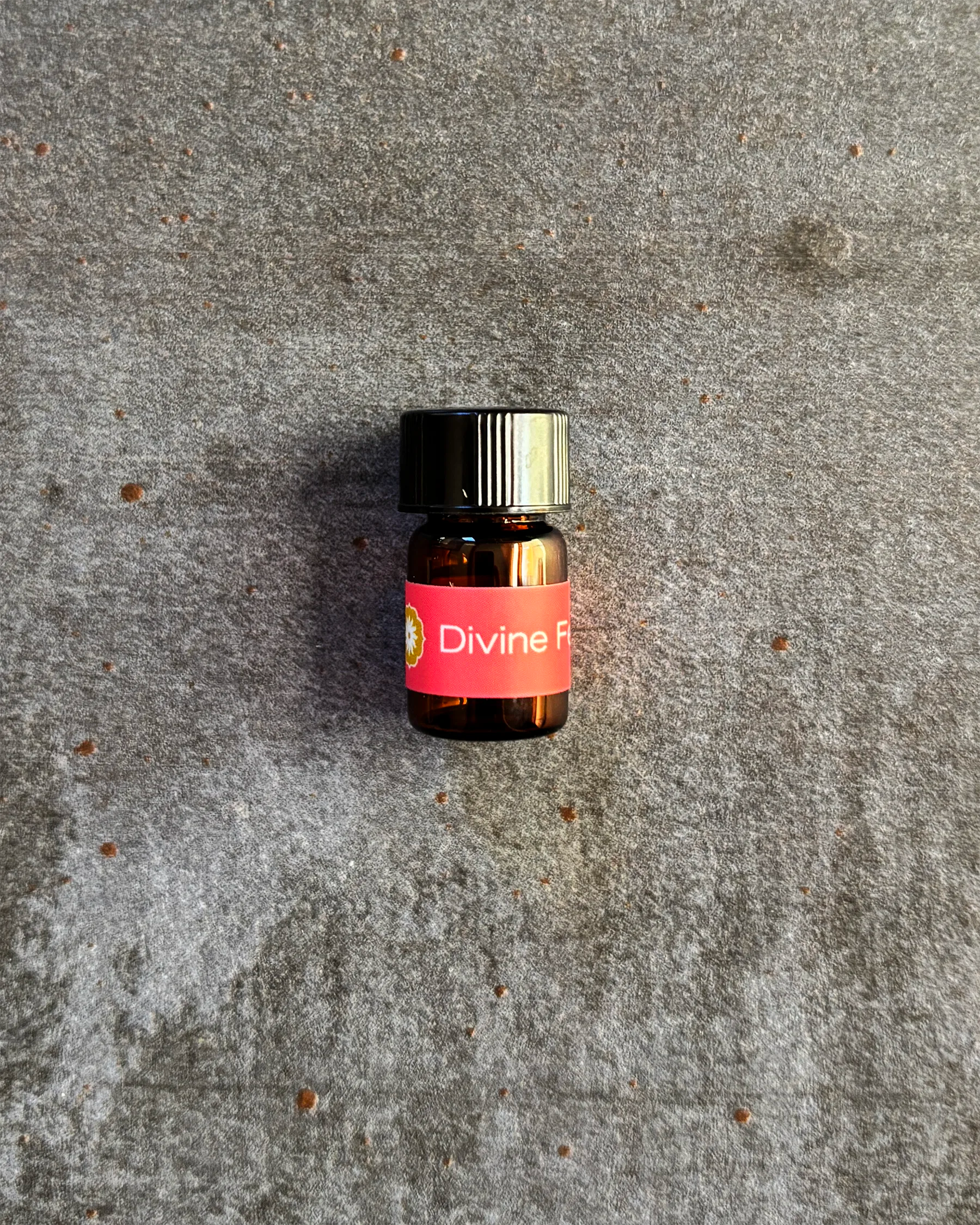 Small amber vial of BodyMantra Divine Feminine oil blend on textured gray stone background.