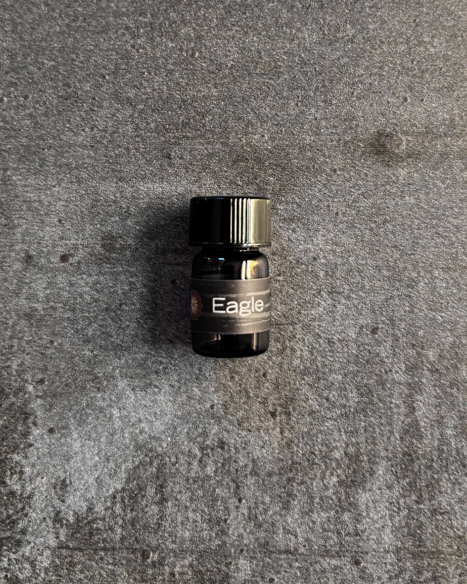 Small amber vial of BodyMantra Eagle Power Animal oil blend on textured gray stone background.