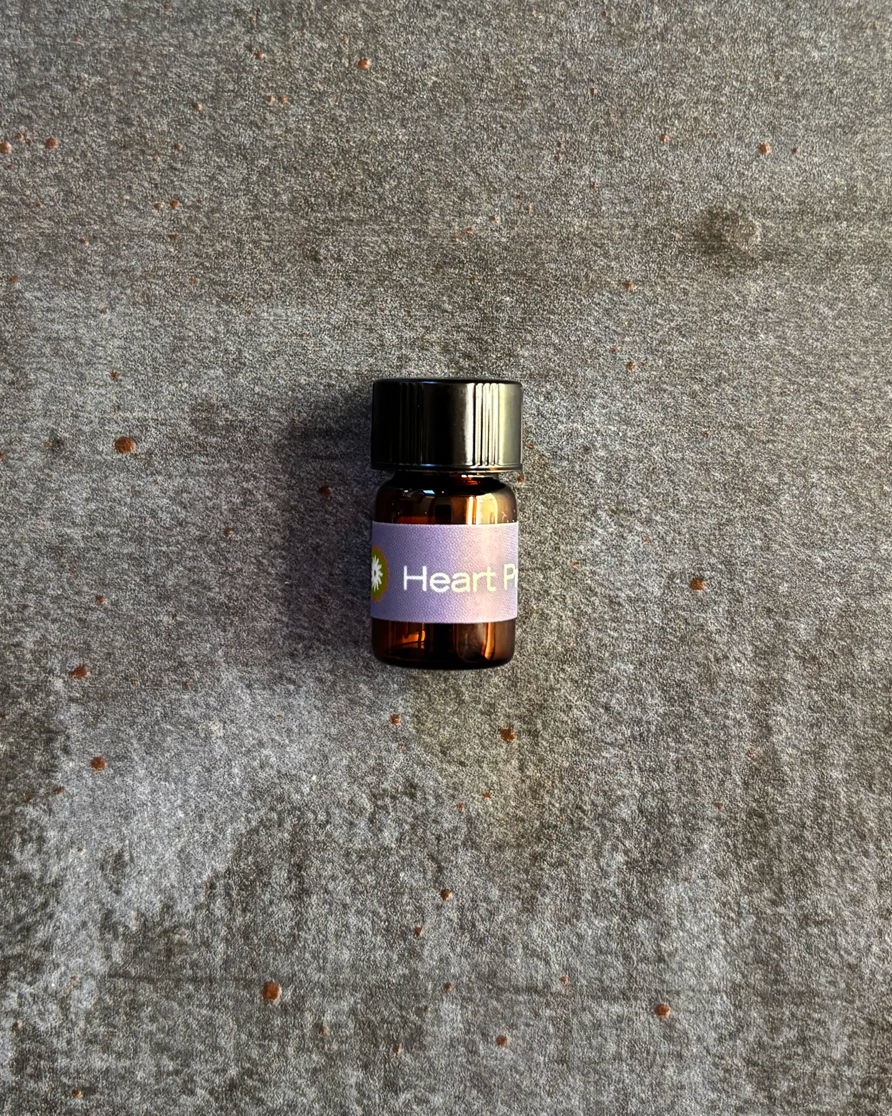 Small amber vial of BodyMantra Heart Presence oil blend on textured gray stone background.