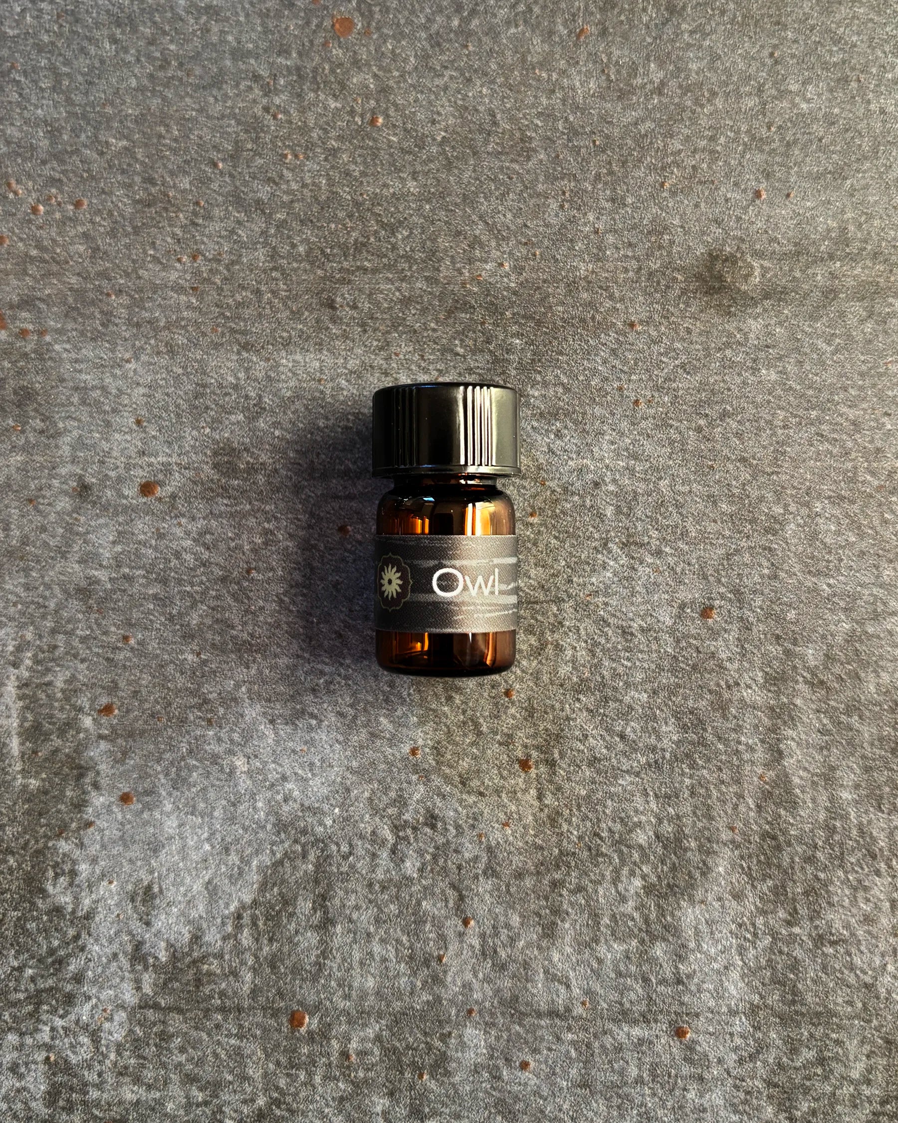 Small amber vial of BodyMantra Owl Power Animal oil blend on textured gray stone background.