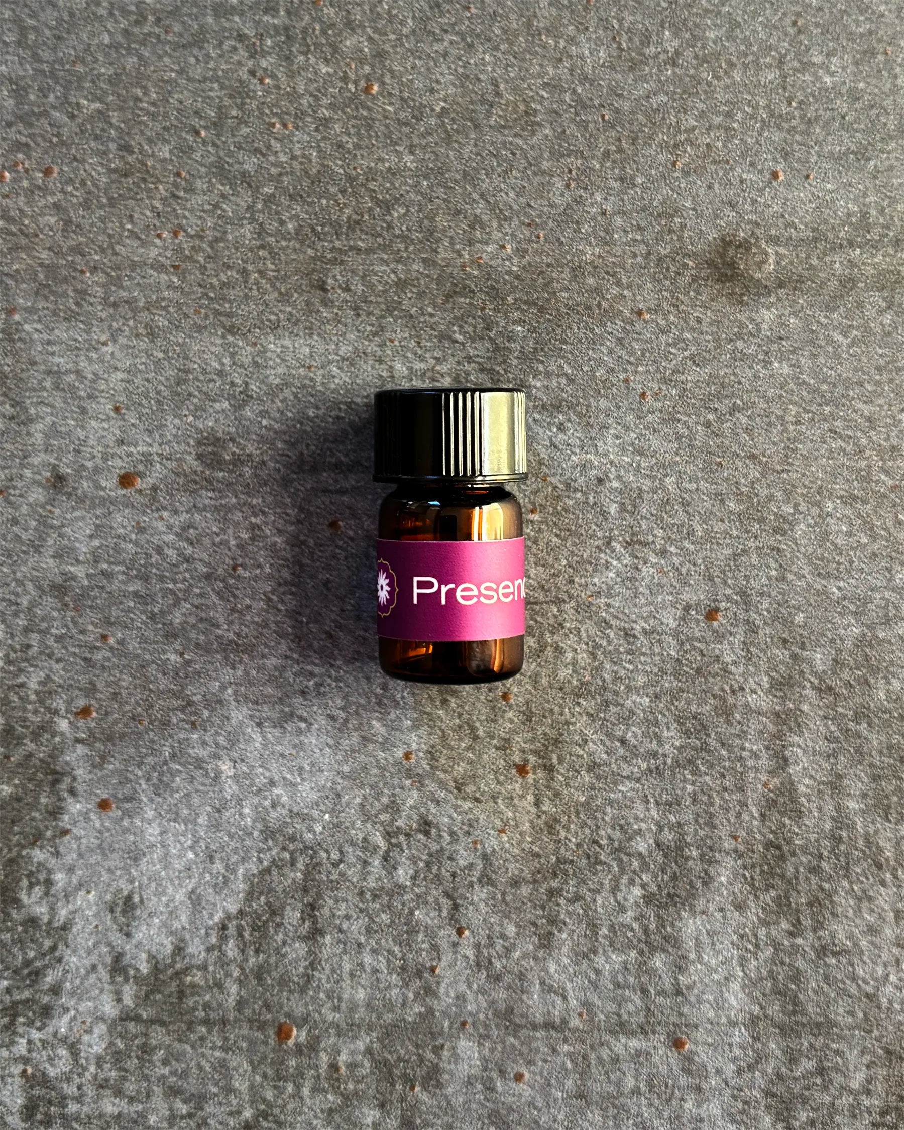 Small amber vial of BodyMantra Presence oil blend on textured gray stone background.