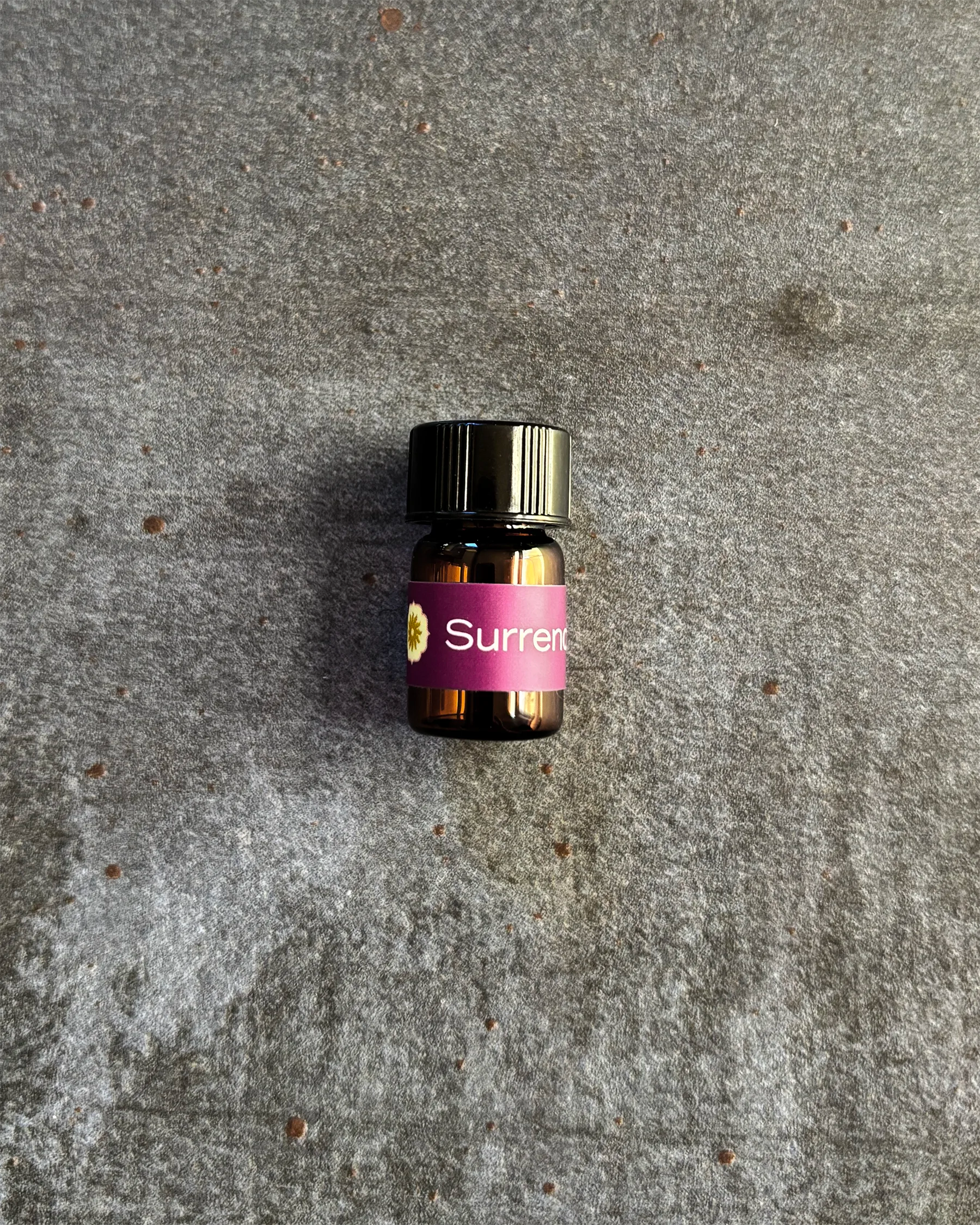 Small amber vial of BodyMantra Surrender oil blend on textured gray stone background.