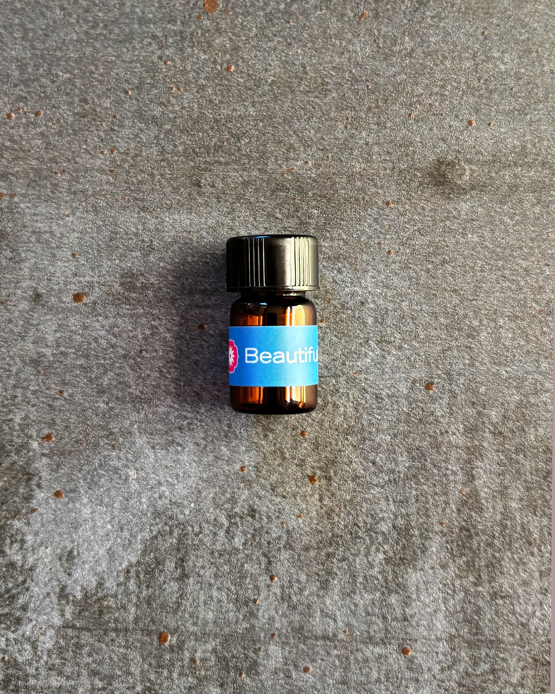 Small amber vial of BodyMantra Beautiful Breast Elixir oil blend on textured gray stone background.