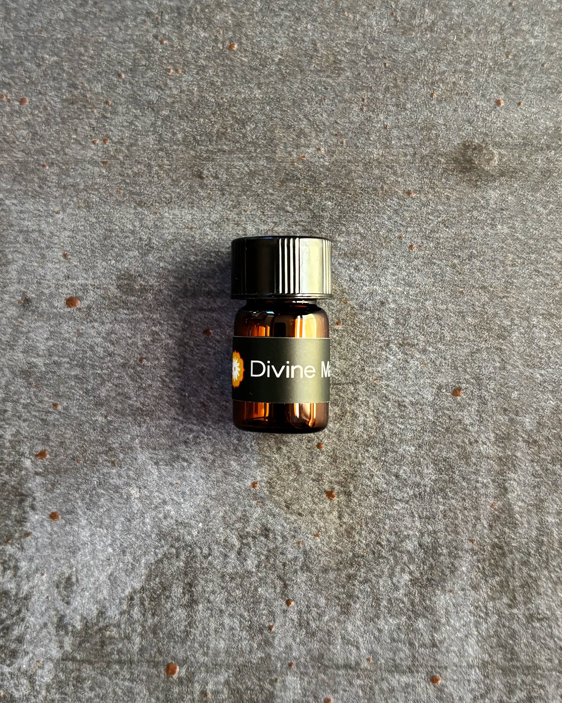 Small amber vial of BodyMantra Divine Masculine oil blend on textured gray stone background.