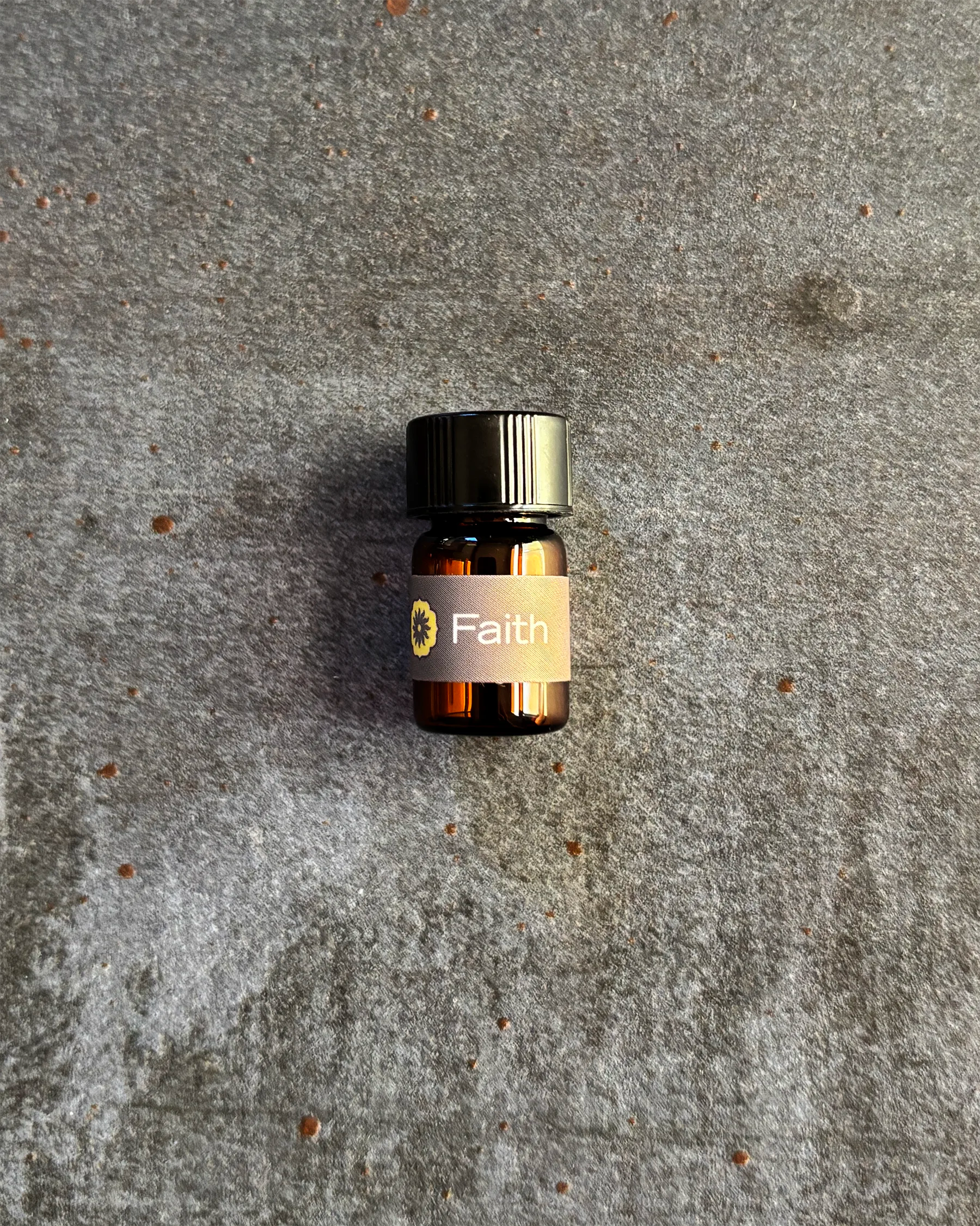 Small amber vial of BodyMantra Faith oil blend on textured gray stone background.
