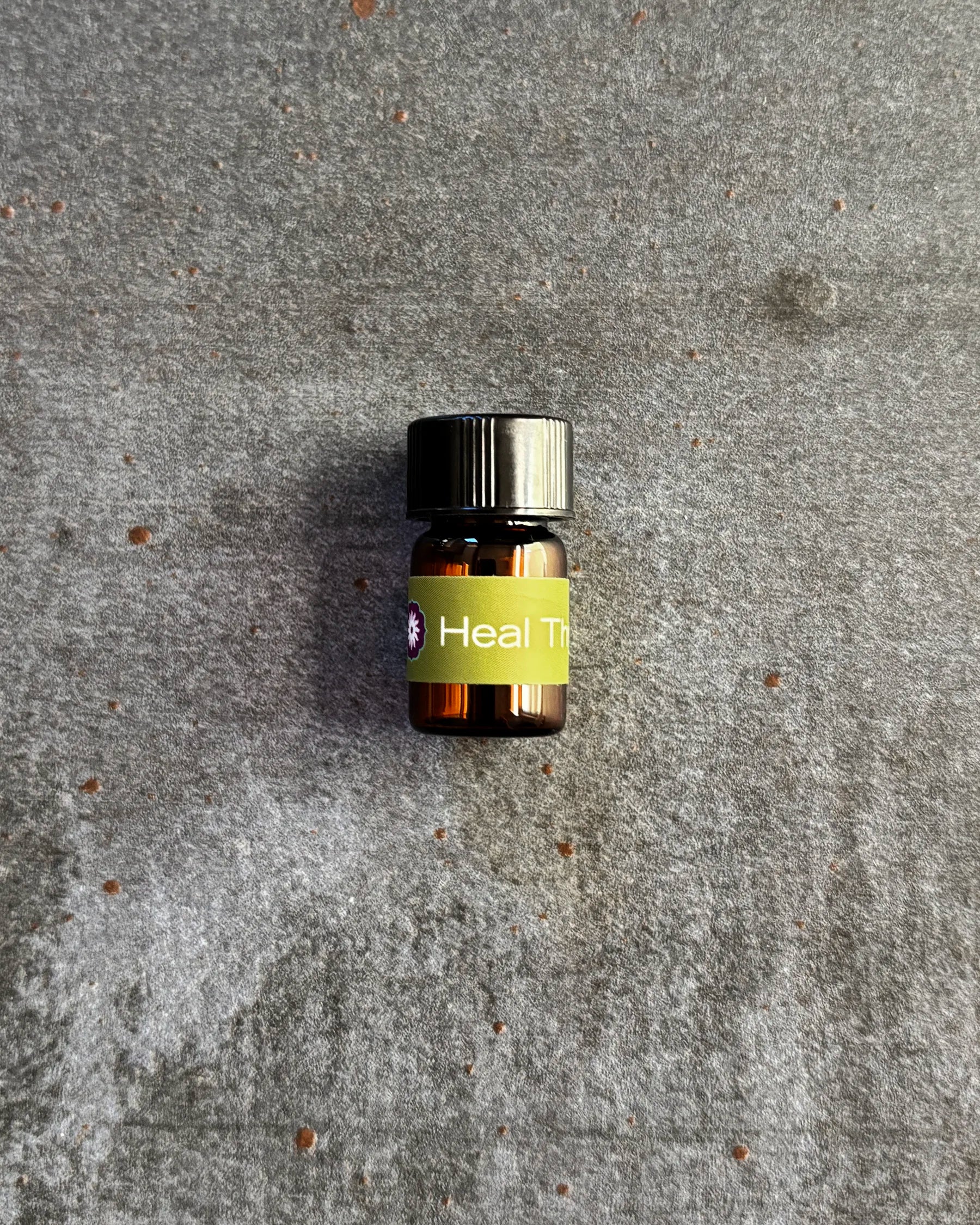 Small amber vial of BodyMantra Heal Thyself oil blend on textured gray stone background.