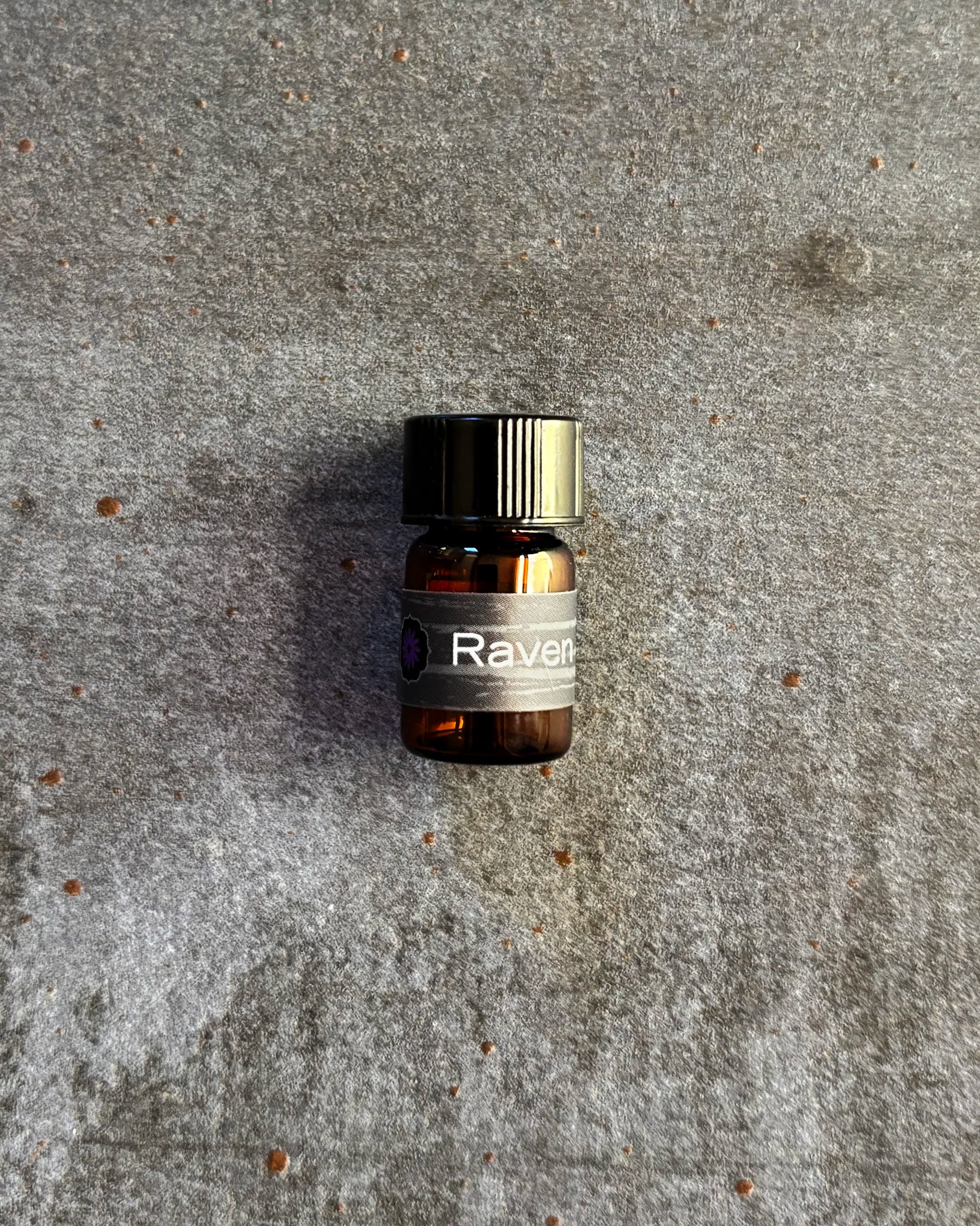 Small amber vial of BodyMantra Raven Power Animal oil blend on textured gray stone background.