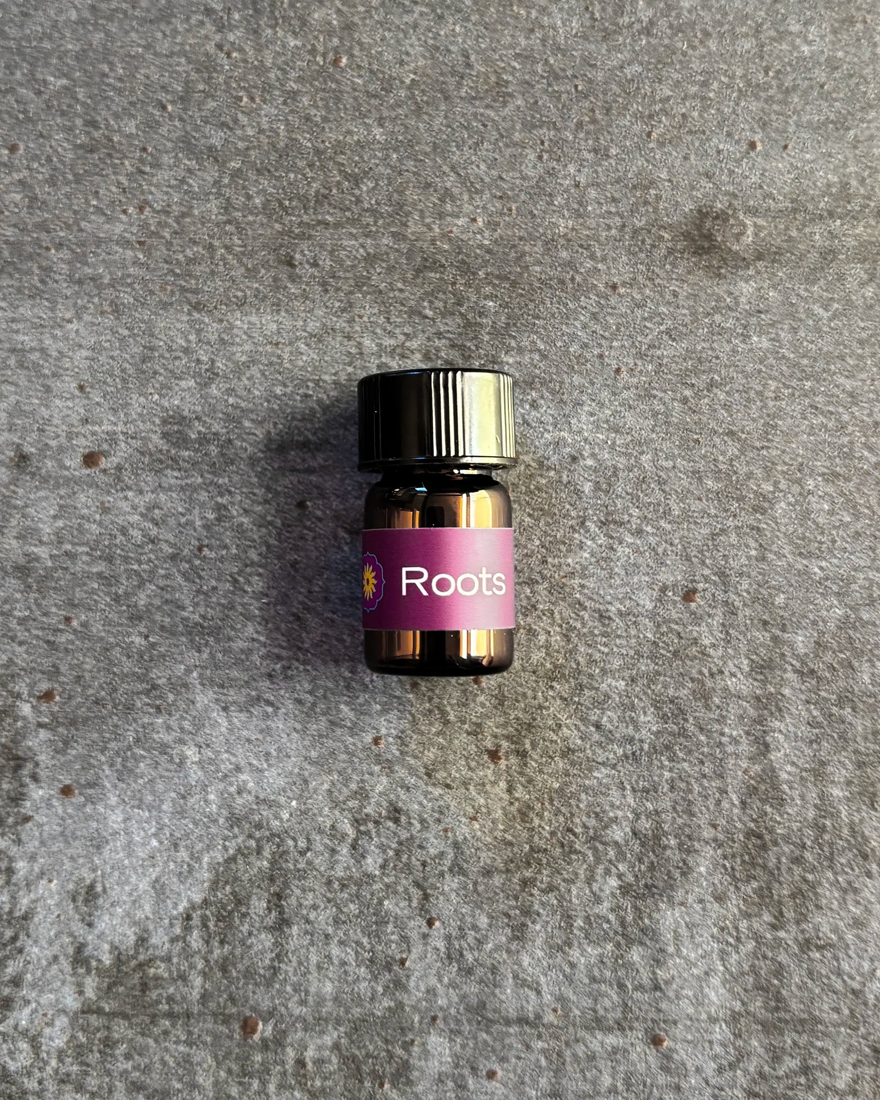 Small amber vial of BodyMantra Roots oil blend on textured gray stone background.