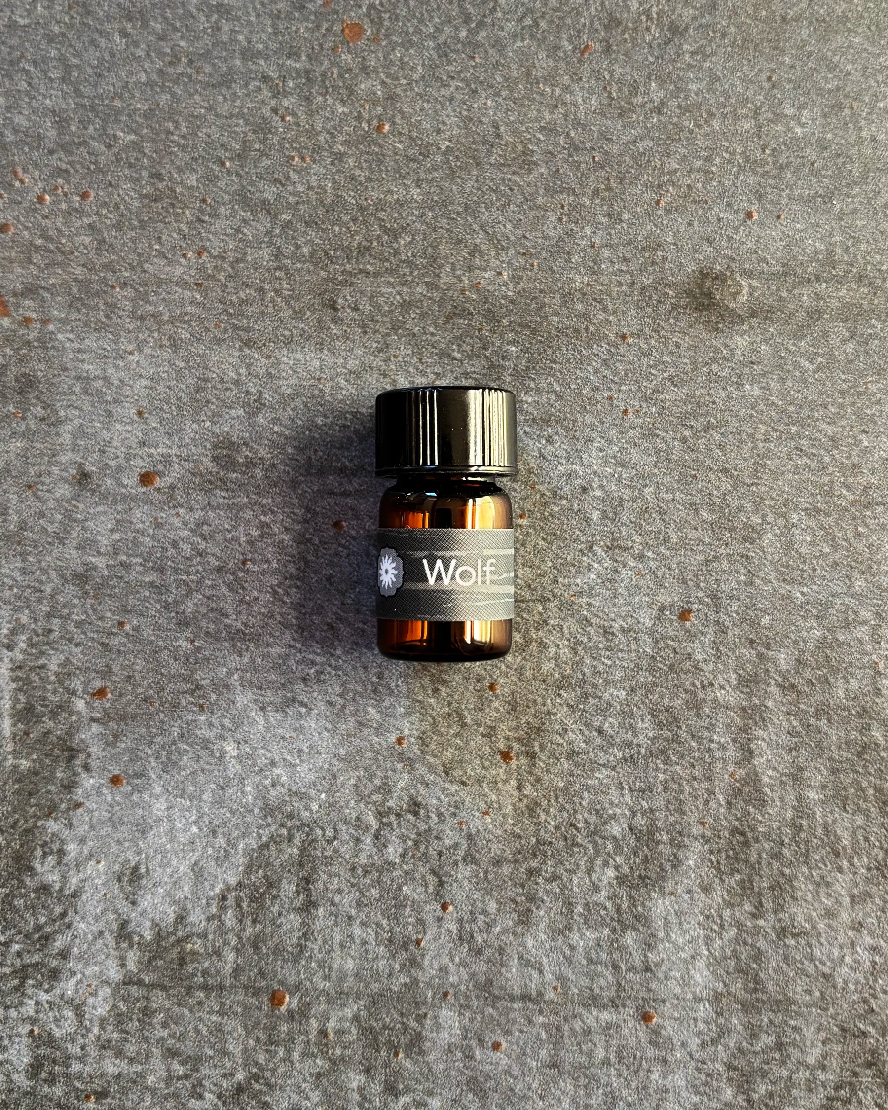 Small amber vial of BodyMantra Wolf Power Animal oil blend on textured gray stone background.